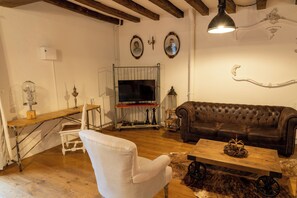 A living room with a brown leather sofa, a white armchair, a wooden coffee table, and a television. - House 3 on the Embourg estate (Souvigny)