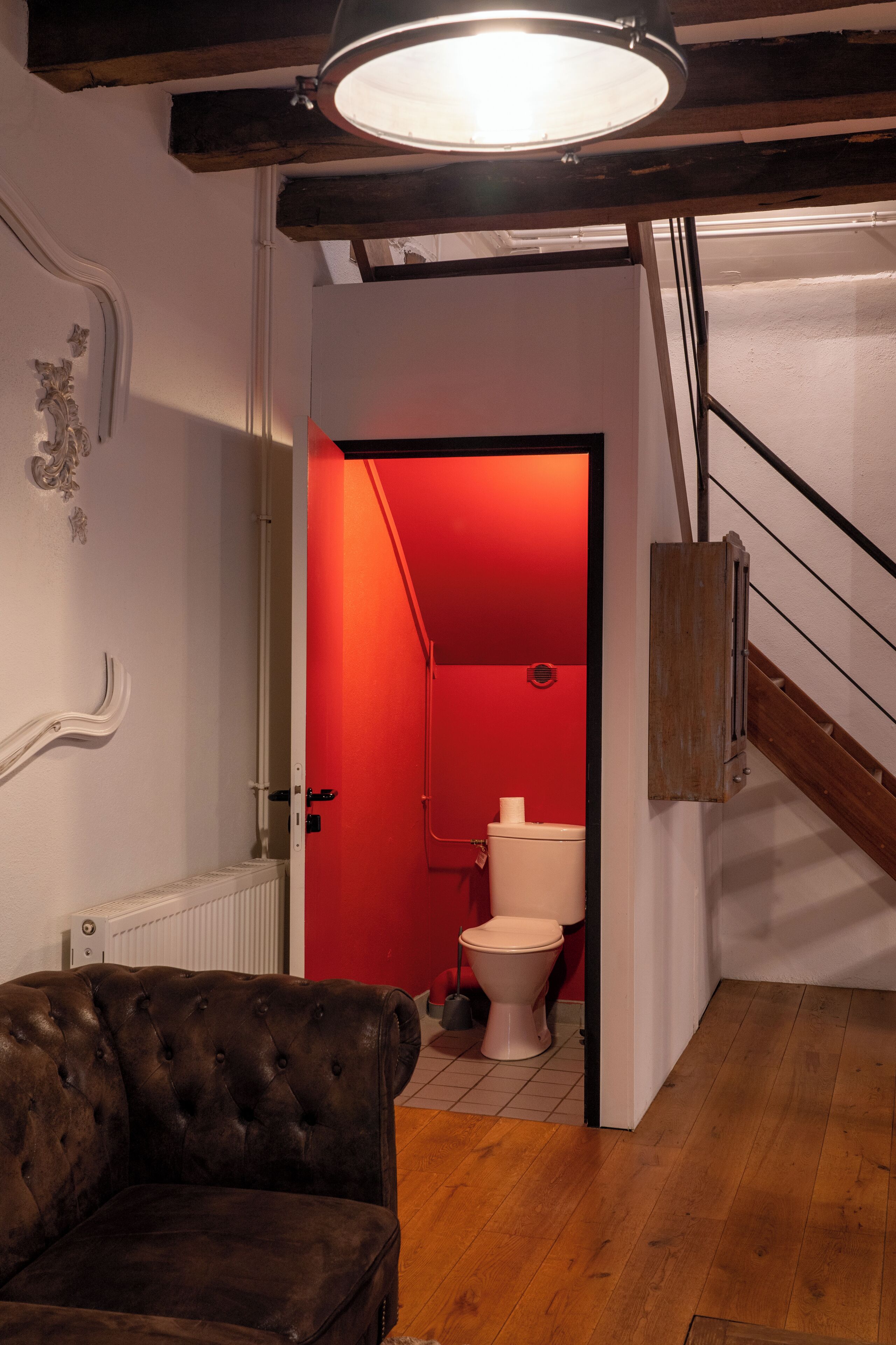Une pièce avec un plancher en bois, un fauteuil en cuir capitonné, un radiateur et une salle de bain éclairée de lumière rouge.