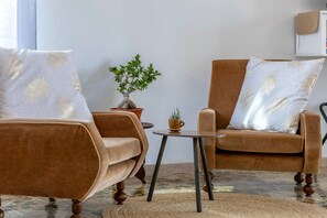 Une pièce comprenant deux fauteuils marron, une petite table ronde, une plante en pot et une étagère fixée au mur.