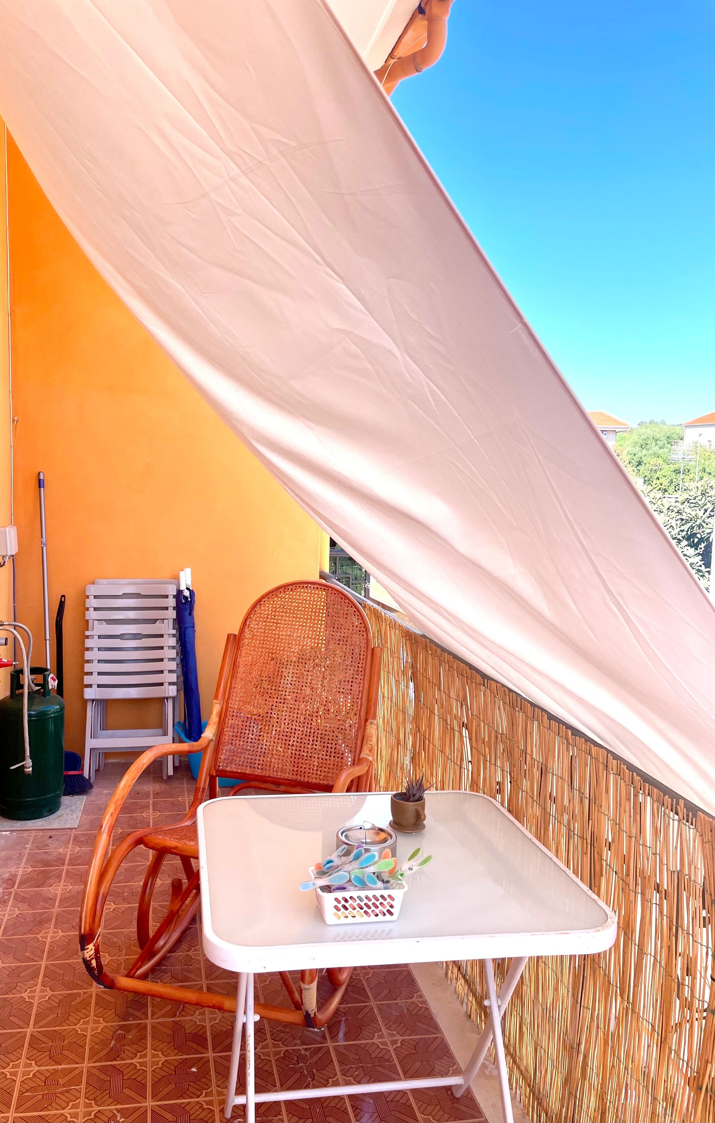 Ein Balkon mit einem Korbstuhl, einem kleinen Tisch mit einer Obstschale und Blick zum Himmel.