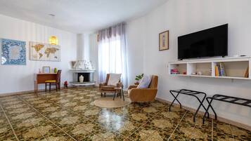 Una sala de estar con piso de baldosas, un televisor de pantalla plana, una chimenea y una estantería.