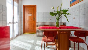 Eine Küche mit einer Holztür, einem Esstisch mit roten Stühlen, einer Blumenvase und einem Bild an der Wand.