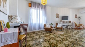 Ein Wohnzimmer mit Fernseher, Sesseln, einem Esstisch und einem gemusterten Boden.