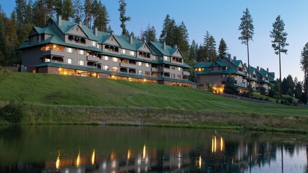 A multi-story hotel with a green roof, located near a body of water and surrounded by trees.