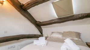Une chambre avec un plafond en pente, des poutres apparentes, un lit recouvert d’une couette beige et deux serviettes enroulées posées sur le lit.