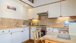 Une cuisine avec des meubles blancs, une table en bois, une cuisinière et un four à micro-ondes.