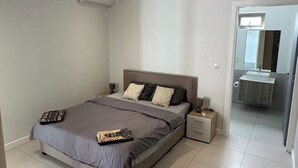 Een slaapkamer met een bed, nachtkastjes, een badkamer met een wastafel en spiegels.