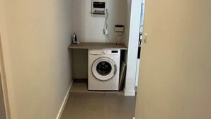 Een kleine wasruimte met een wasmachine, een klein aanrecht en een wandbeugelverwarming.