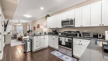 A modern kitchen with white cabinets, stainless steel appliances, and a wooden floor.