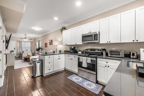 A modern kitchen with white cabinets, stainless steel appliances, and a wooden floor.
