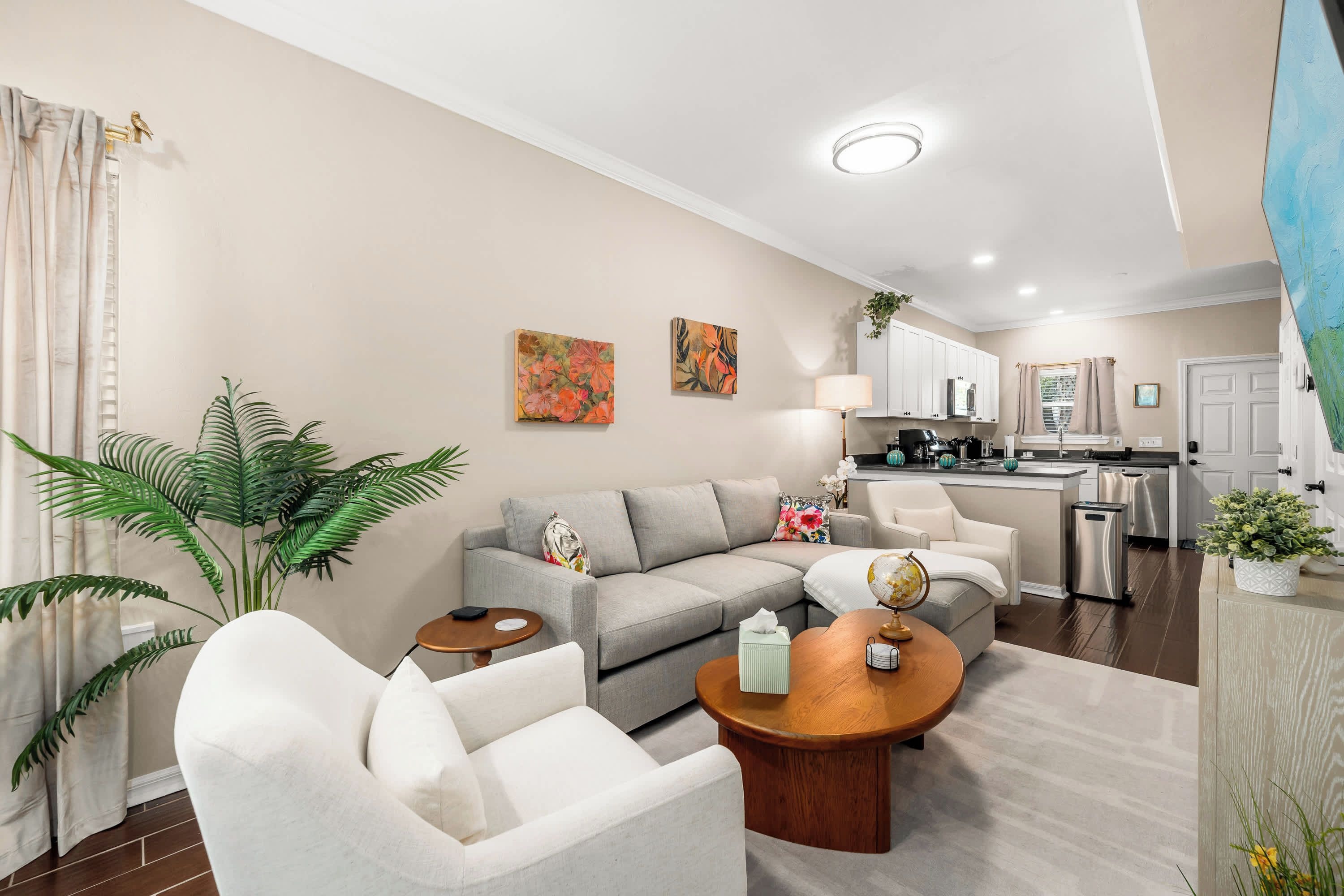 Un salon moderne avec un canapé gris, un fauteuil blanc, une table basse et un coin repas avec une cuisine en arrière-plan.