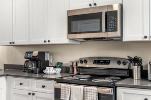 Une cuisine moderne avec des meubles blancs, un four à micro-ondes en acier inoxydable, une machine à café et une cuisinière.