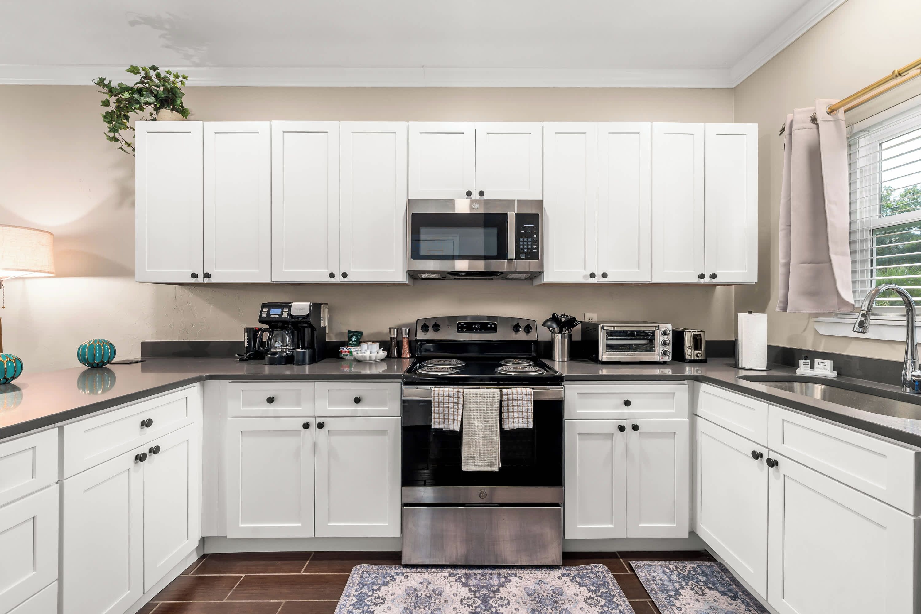 A modern kitchen with white cabinets, a microwave, a stove, and a coffee maker.