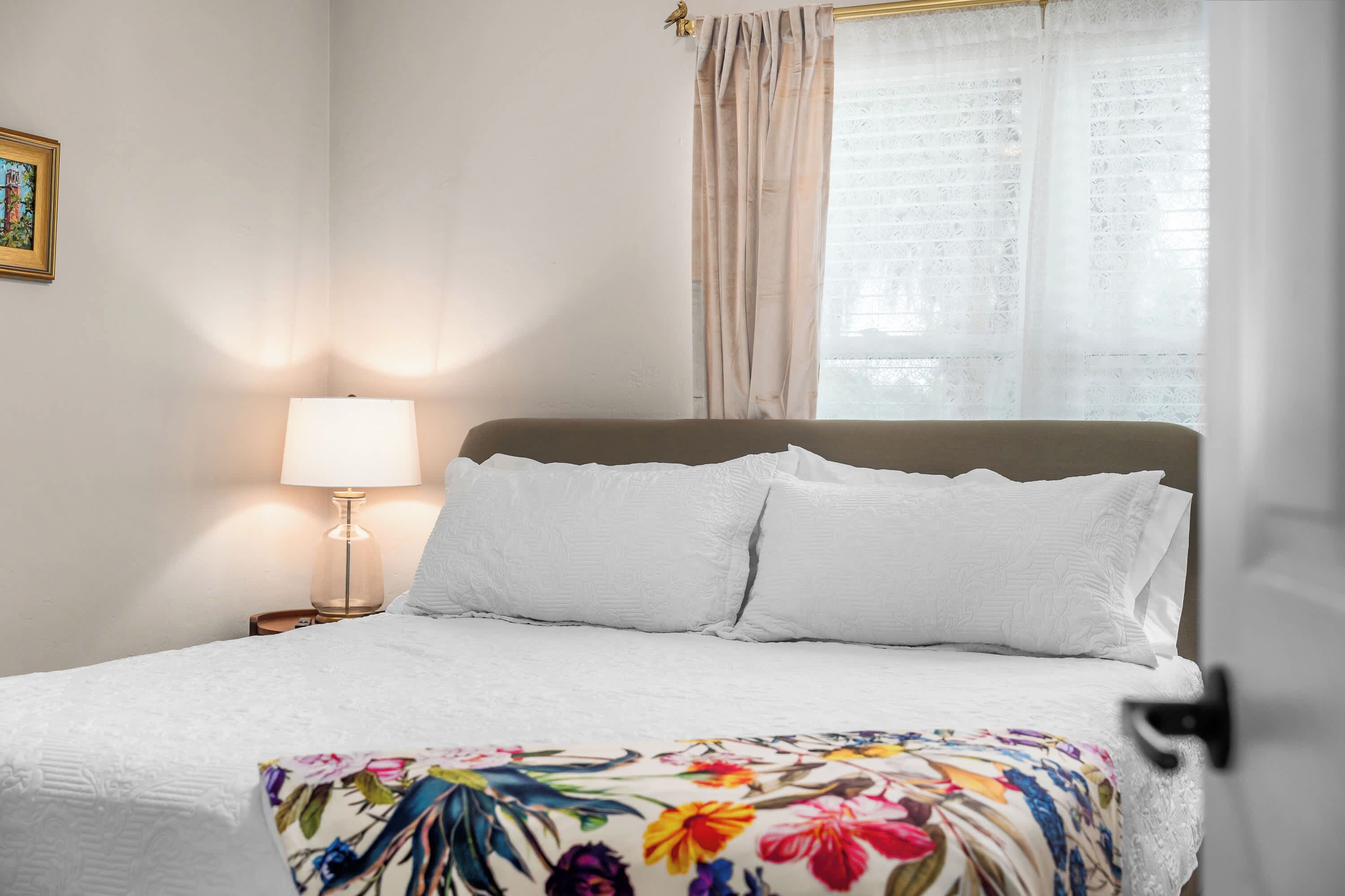 Un lit bien fait, avec du linge de lit blanc, un plaid à motifs floraux et une lampe de chevet.