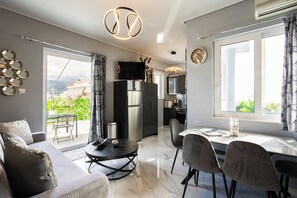 A modern living room with a sofa, dining table, and chairs, a kitchen area with a refrigerator, and a balcony with a view. - Kalamata Coastal Nest, Modern Seaside Escape (Kalamata)
