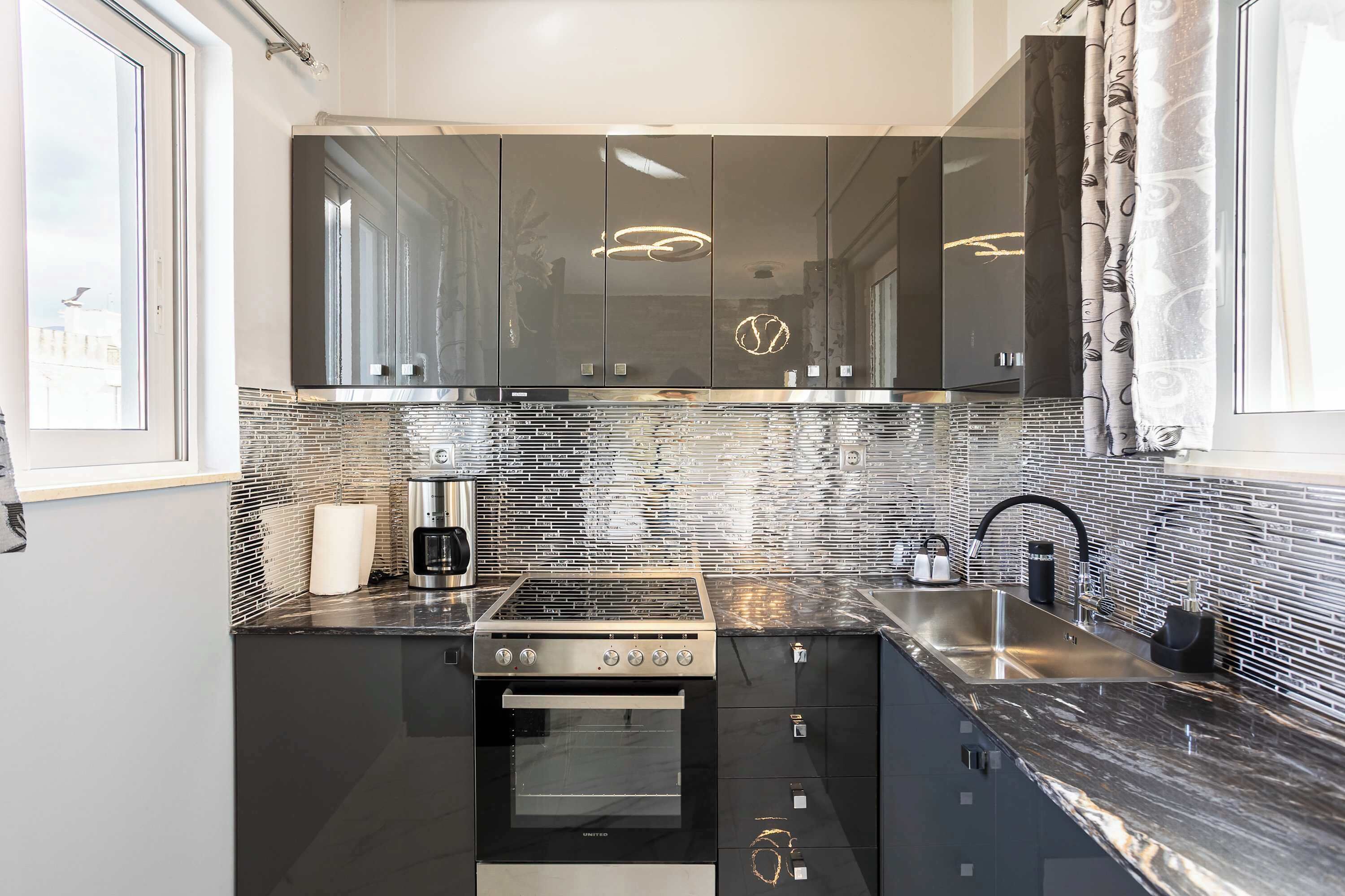 A modern kitchen with a built-in oven, stainless steel sink, and black cabinets.