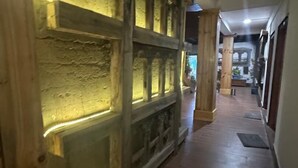 Un couloir aux murs lambrés et recouverts de pierres, qui mène à une pièce comprenant un lit et une table de chevet.