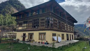 Un bâtiment traditionnel à plusieurs étages, doté d’un balcon, qui se dresse sur un fond de paysage montagneux.