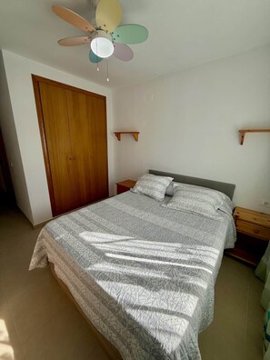 A bedroom with a bed, a wooden wardrobe, a ceiling fan, and a nightstand.