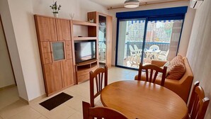 Un espace de vie compact comprenant un coin repas, une kitchenette et une porte-fenêtre coulissante donnant sur une terrasse extérieure.