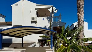 Un bâtiment blanc avec un auvent bleu, une terrasse carrelée et un palmier.