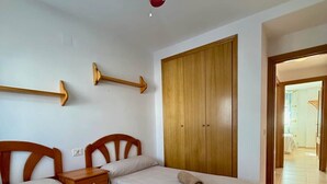 Une chambre avec deux lits, une armoire en bois, un ventilateur de plafond et une table de chevet.