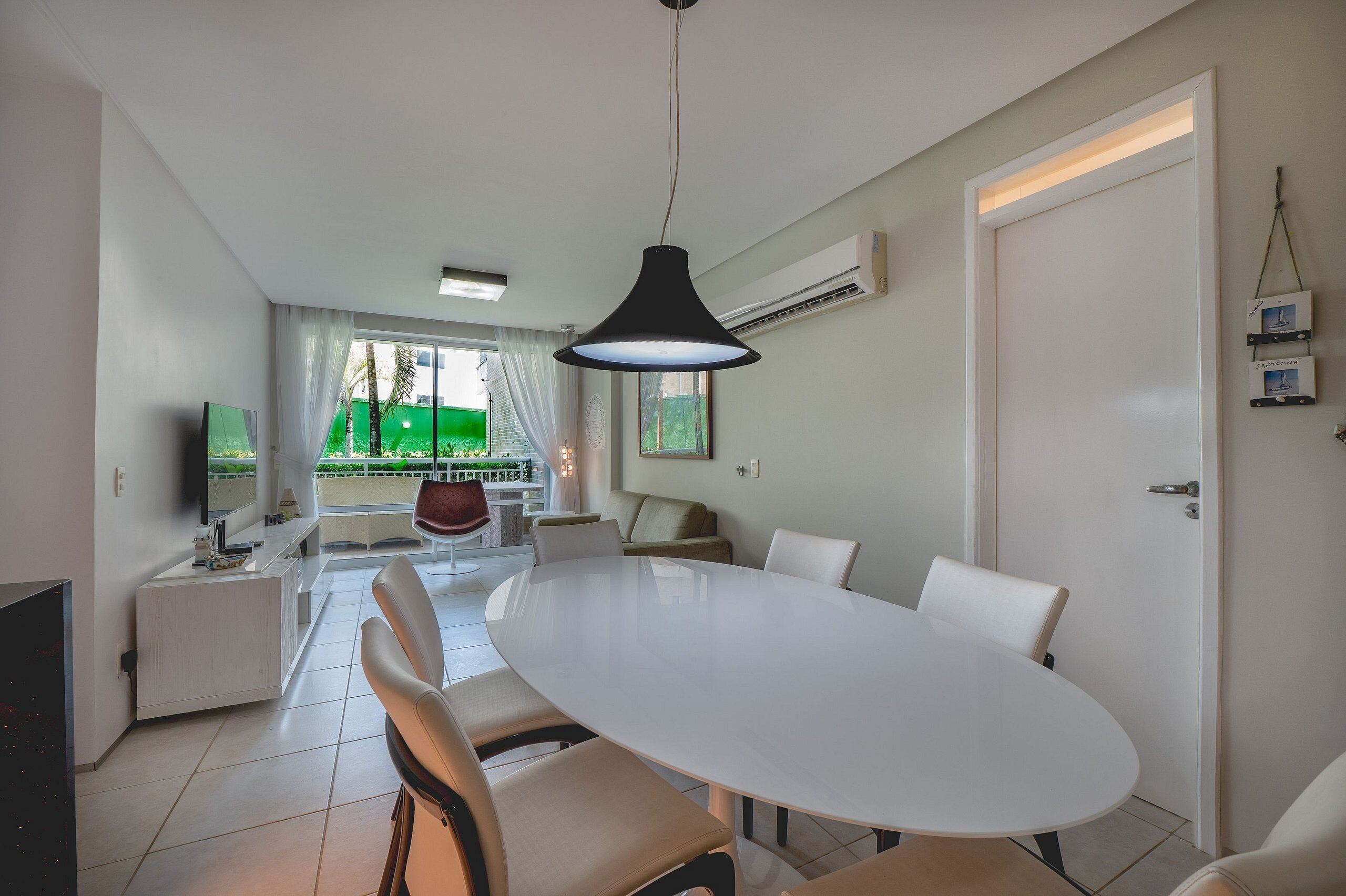 A modern dining area with a large oval table, white chairs, and a black pendant light.