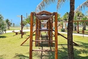 A wooden climbing structure in a park with palm trees and a clear blue sky.