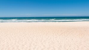 Ein weiter Sandstrand mit sanften Wellen und blauem Himmel.