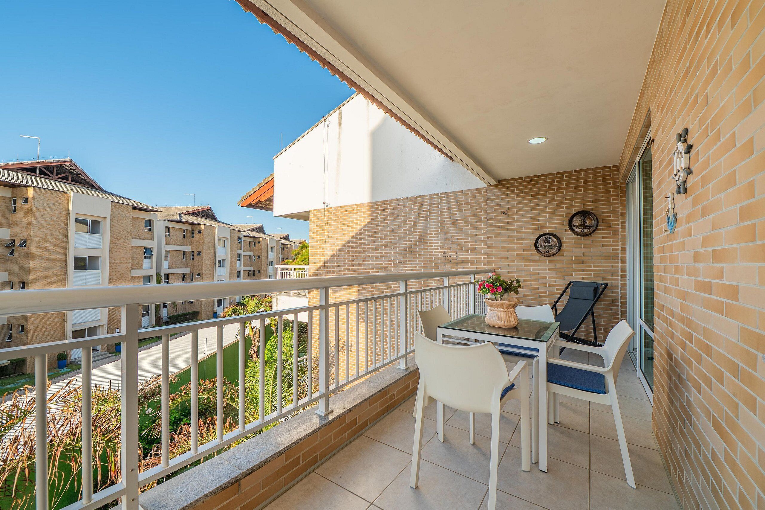 A balcony with a table and chairs, a potted plant, and a view of neighboring buildings.
