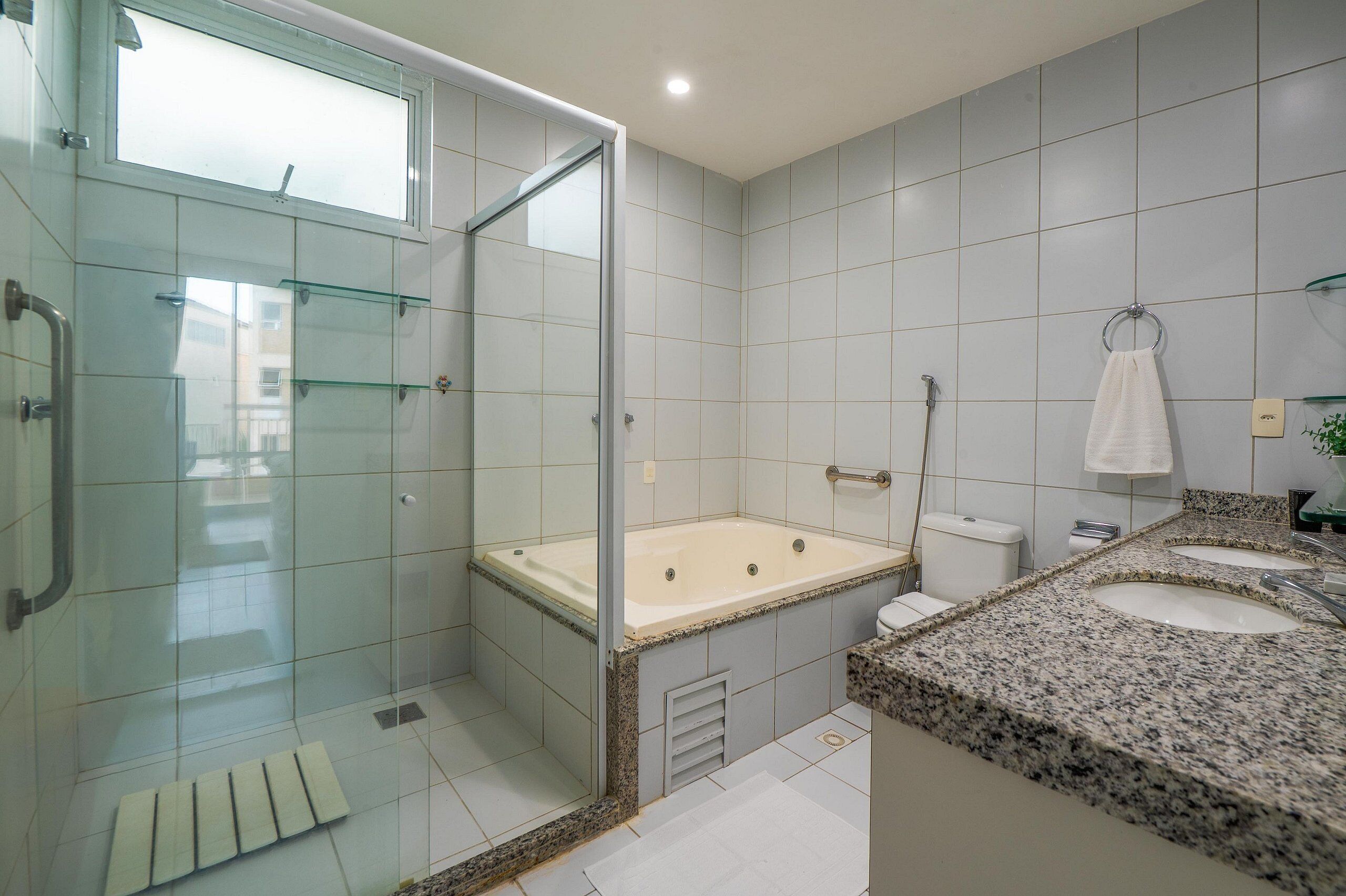Een moderne badkamer met een douchecabine van glas, een vrijstaand bad en een granieten aanrecht met twee wasbakken.