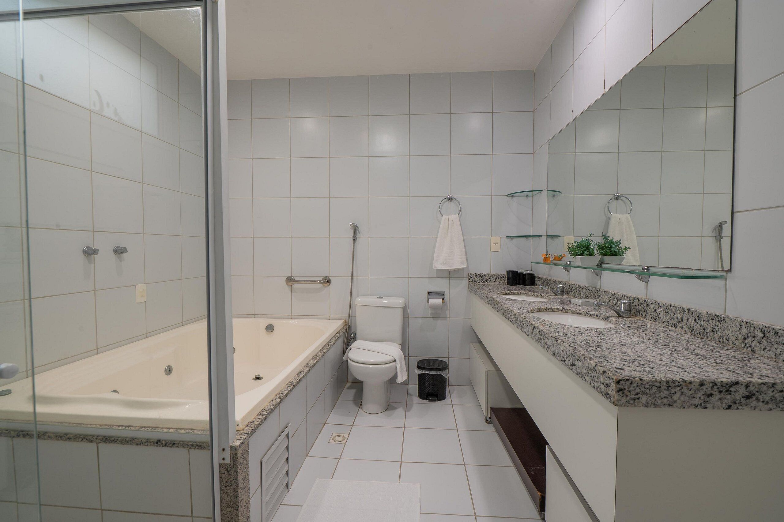 Une salle de bain moderne dotée d’une douche à parois de verre, d’une baignoire, de toilettes et d’un meuble-lavabo avec un plan de travail en granit.