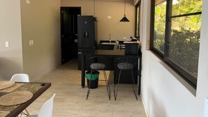 Eine kleine Küche mit Essbereich, einem schwarzen Kühlschrank und einem Fenster mit Blick auf Grünflächen.