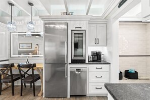 A modern kitchen with stainless steel appliances, a dishwasher, and a dining area with wooden chairs. - Gulf-Front Beachfront Condo w/ Pool | Walk to Dini (Panama City Beach)