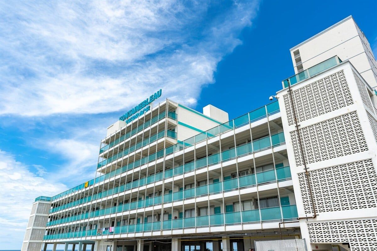 A multi-story hotel with a modern architectural design, featuring balconies and a clear sky in the background.