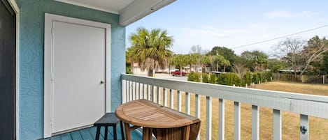 A covered porch with a table and chairs, a door, and a view of a residential area with trees and a parked car.