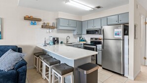 A modern kitchen with grey cabinets, a stainless steel refrigerator, a built-in oven, and a central island with bar stools. - Pet-Friendly 2BR | Walk to the Beach | Pool (Panama City Beach)