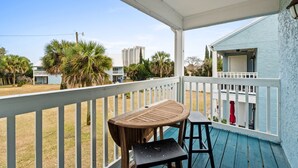 A covered outdoor area with a wooden table and two chairs, a white railing, and a view of a building and palm trees. - Pet-Friendly 2BR | Walk to the Beach | Pool (Panama City Beach)