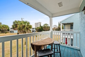 A covered outdoor area with a table and chairs, a view of a building, and palm trees. - Pet-Friendly 2BR | Walk to the Beach | Pool (Panama City Beach)