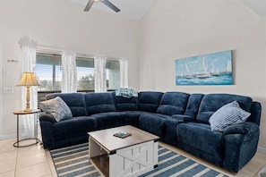 A living room with a dark blue sectional sofa, a small wooden coffee table, a striped rug, a floor lamp, and a painting of sailboats on the wall. - Pet-Friendly 2BR | Walk to the Beach | Pool (Panama City Beach)