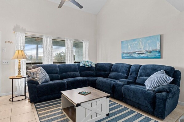A living room with a dark blue sectional sofa, a small wooden coffee table, a striped rug, a floor lamp, and a painting of sailboats on the wall. - Pet-Friendly 2BR | Walk to the Beach | Pool (Panama City Beach)