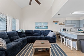 A living room with a dark blue sectional sofa, a wooden coffee table, and a painting of sailboats on the wall. - Pet-Friendly 2BR | Walk to the Beach | Pool (Panama City Beach)