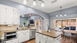 Une cuisine moderne avec des meubles blancs, un îlot central en bois et un coin repas offrant une vue agréable.
