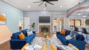 Un salon avec deux canapés bleus, un fauteuil jaune, une cheminée et un ventilateur de plafond.