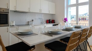 A modern kitchen with white cabinets, a marble countertop, and a dining area with wicker chairs and a white table set for four.