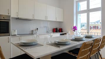 Une cuisine moderne avec des meubles blancs, un plan de travail en marbre et un coin repas comprenant des chaises en osier et une table blanche dressée pour quatre personnes.