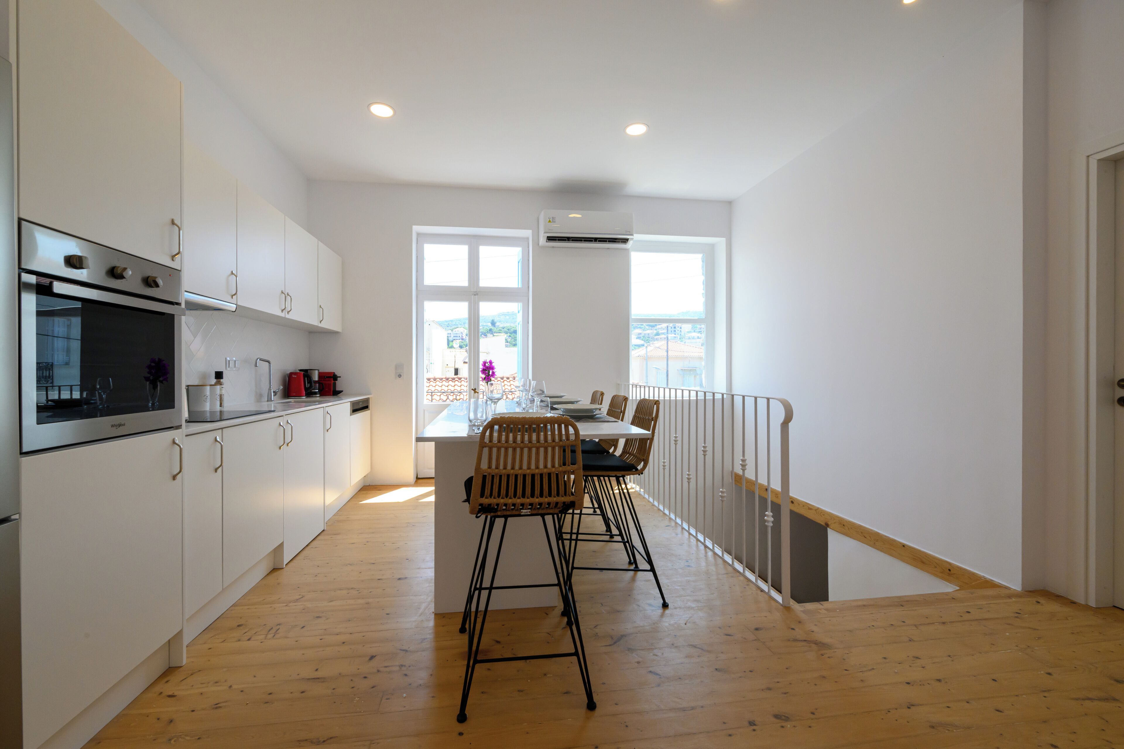 A modern kitchen with white cabinets, a built-in oven, and a dining area with a wooden table and chairs.