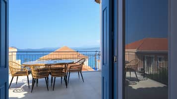 Un balcon avec une table et des chaises, une vue sur la mer et un bâtiment avec un toit rouge.