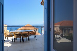 Ein Balkon mit Tisch und Stühlen, Blick auf das Meer und ein Gebäude mit rotem Dach.