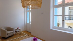 A bedroom with a bed, a chair, a small table, and a hanging light fixture.